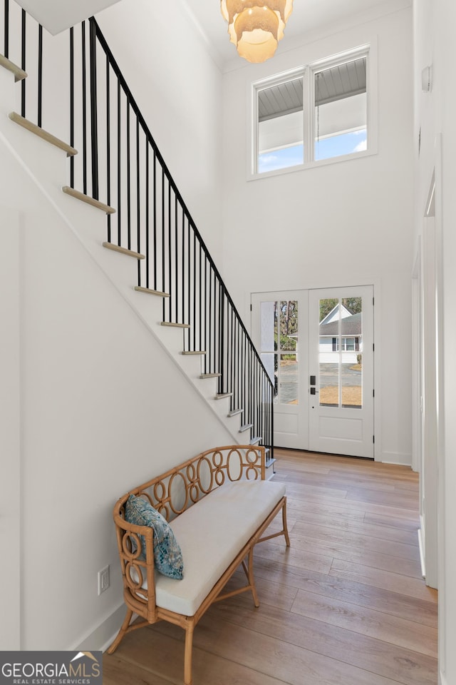 foyer entrance with a high ceiling, crown molding, light wood-type flooring, and french doors