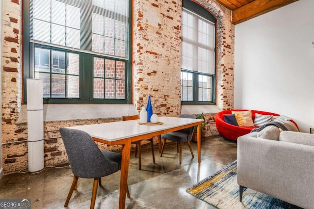 dining area with a towering ceiling, brick wall, and concrete floors