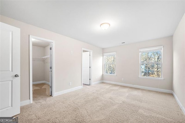 unfurnished bedroom with light carpet, a walk in closet, and a closet