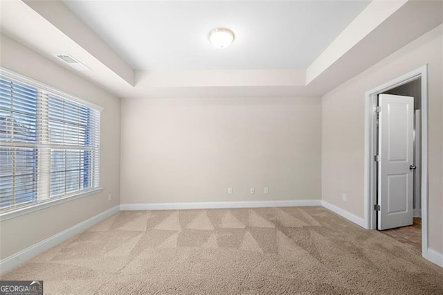 unfurnished room with light colored carpet and a tray ceiling