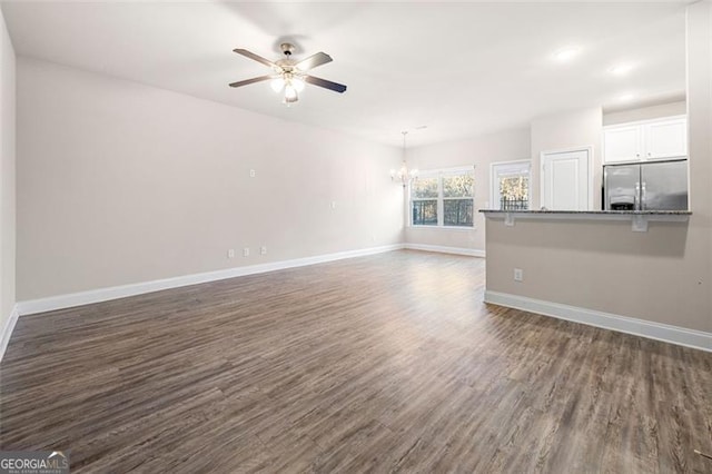 unfurnished living room with ceiling fan with notable chandelier and dark hardwood / wood-style flooring