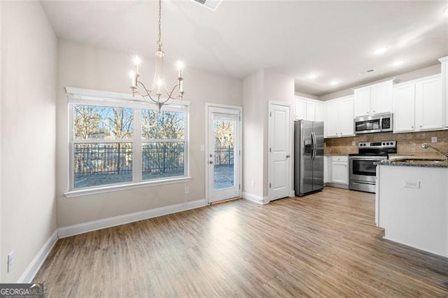 kitchen with pendant lighting, backsplash, white cabinets, and appliances with stainless steel finishes