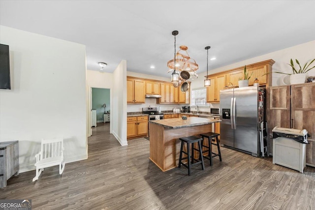 kitchen with a breakfast bar area, a center island, hanging light fixtures, appliances with stainless steel finishes, and dark hardwood / wood-style flooring