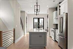 kitchen with white cabinetry, a kitchen island with sink, high end appliances, decorative light fixtures, and light wood-type flooring