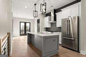 kitchen featuring pendant lighting, an island with sink, white cabinetry, high end refrigerator, and wall chimney range hood