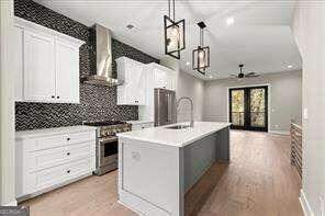 kitchen with wall chimney exhaust hood, pendant lighting, an island with sink, high end stainless steel range oven, and white cabinets