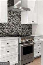 kitchen featuring wall chimney range hood, white cabinets, backsplash, and high end stove