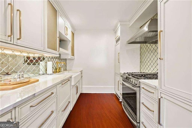 kitchen featuring wall chimney exhaust hood, tasteful backsplash, dark hardwood / wood-style floors, stainless steel range with gas stovetop, and light stone countertops