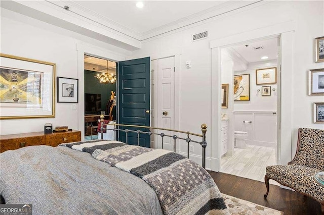 bedroom with connected bathroom, hardwood / wood-style floors, crown molding, and a chandelier