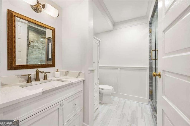 bathroom with ornamental molding, toilet, vanity, and a shower with shower door