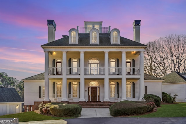 neoclassical home featuring a porch, a balcony, and a lawn