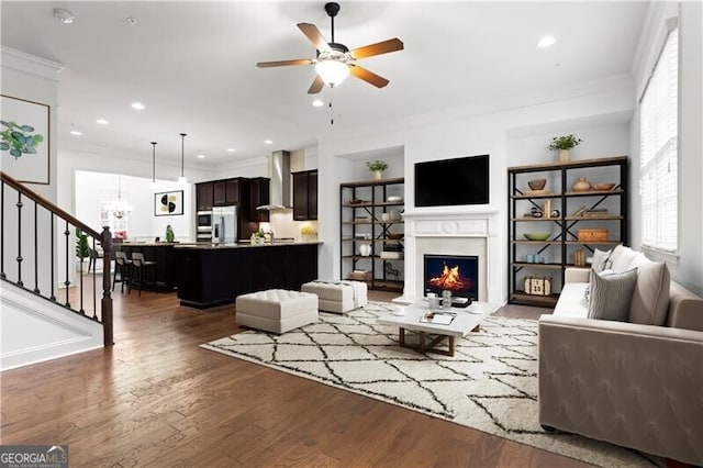 living area featuring stairway, wood finished floors, a warm lit fireplace, and ornamental molding