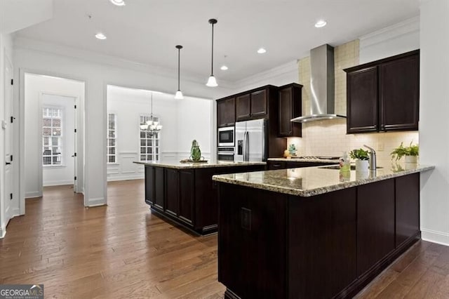 kitchen with dark wood-style floors, ornamental molding, stainless steel appliances, wall chimney exhaust hood, and a center island