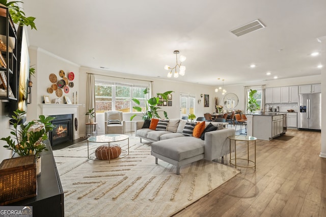 living room with ornamental molding, sink, light hardwood / wood-style flooring, and a notable chandelier