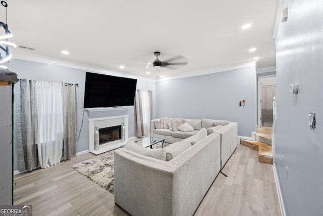 living room featuring ornamental molding, a fireplace, ceiling fan, and light hardwood / wood-style flooring