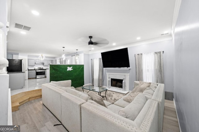 living room with ceiling fan, ornamental molding, a premium fireplace, and light hardwood / wood-style flooring