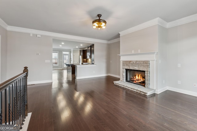 unfurnished living room featuring crown molding, baseboards, a stone fireplace, and dark wood finished floors