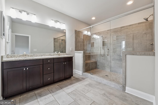 full bathroom with baseboards, a sink, double vanity, and a stall shower