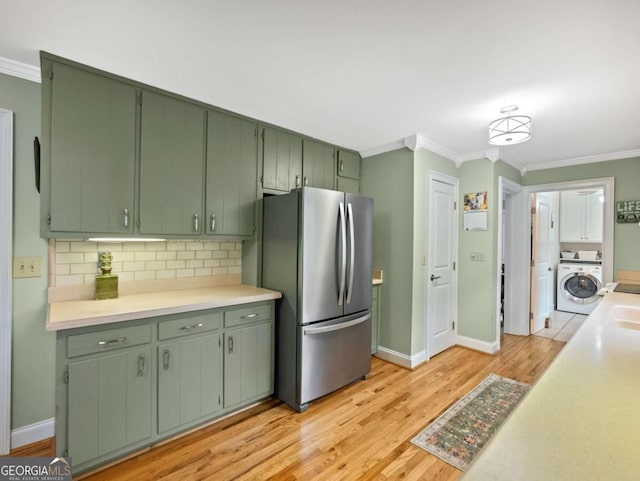 kitchen featuring stainless steel refrigerator, green cabinets, ornamental molding, washer / clothes dryer, and light wood-type flooring