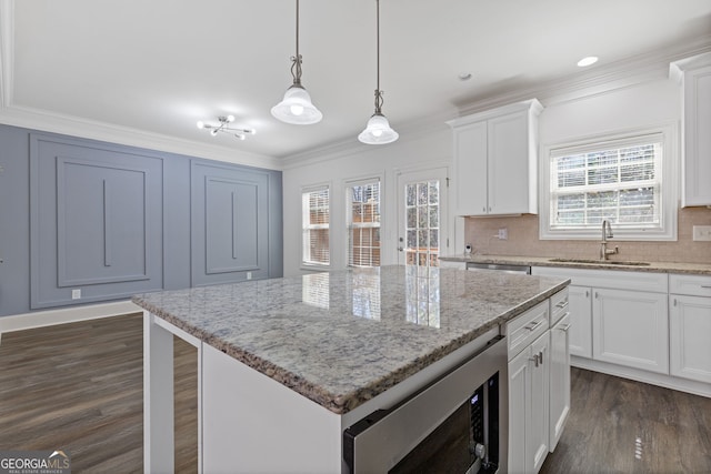 kitchen with white cabinets, a center island, hanging light fixtures, stainless steel appliances, and a sink