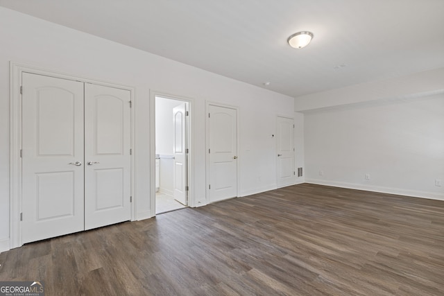 unfurnished bedroom featuring dark wood-style flooring, baseboards, and ensuite bathroom