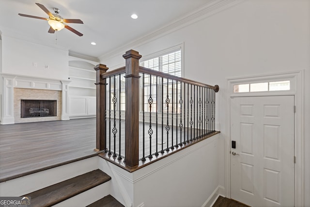 stairs featuring a ceiling fan, wood finished floors, crown molding, a fireplace, and recessed lighting