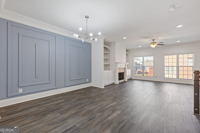 unfurnished living room featuring ceiling fan with notable chandelier, a fireplace, baseboards, dark wood-style floors, and crown molding