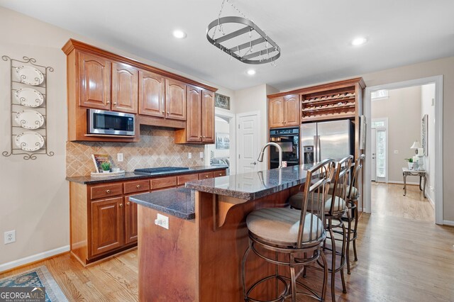 kitchen featuring a breakfast bar area, stainless steel appliances, light hardwood / wood-style floors, an island with sink, and decorative backsplash