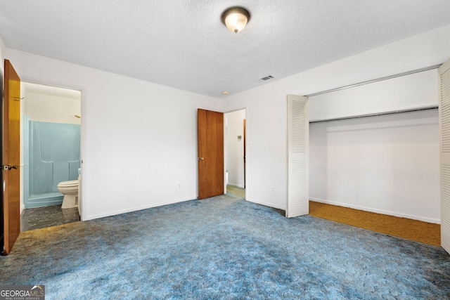 unfurnished bedroom with connected bathroom, a textured ceiling, dark carpet, and a closet