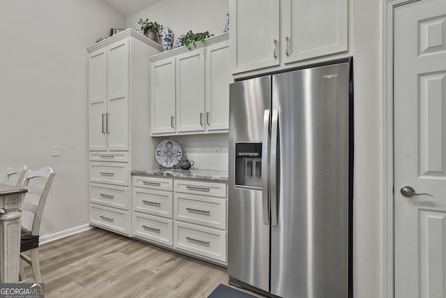 kitchen with stainless steel fridge, light stone counters, light hardwood / wood-style floors, white cabinets, and decorative backsplash