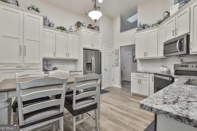 kitchen with pendant lighting, backsplash, appliances with stainless steel finishes, light wood-style floors, and white cabinetry