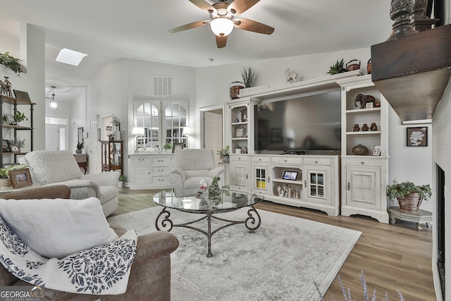 living room featuring ceiling fan, wood-type flooring, and lofted ceiling with skylight