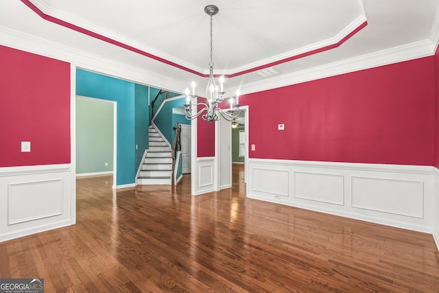 unfurnished dining area featuring a chandelier, wood finished floors, visible vents, stairway, and a tray ceiling