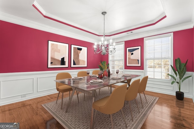 dining space featuring a wainscoted wall, wood finished floors, a raised ceiling, and an inviting chandelier