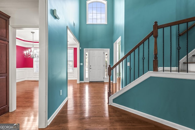 foyer entrance with stairs, a wainscoted wall, wood finished floors, and an inviting chandelier