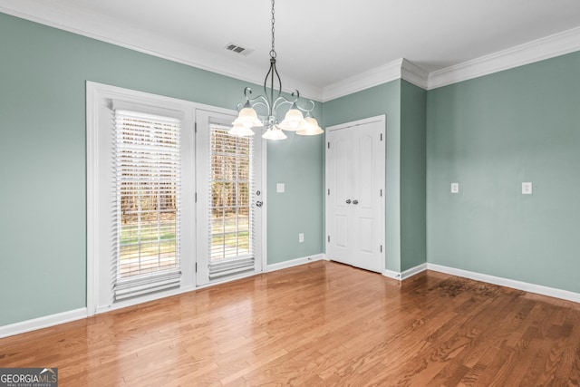 unfurnished dining area featuring baseboards, visible vents, wood finished floors, crown molding, and a notable chandelier