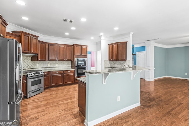 kitchen featuring visible vents, light wood-style flooring, appliances with stainless steel finishes, a breakfast bar area, and ornate columns