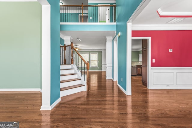 foyer entrance with crown molding, decorative columns, stairway, wainscoting, and wood finished floors