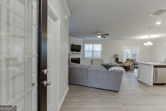 living area featuring visible vents, crown molding, light wood-style floors, a fireplace, and ceiling fan with notable chandelier