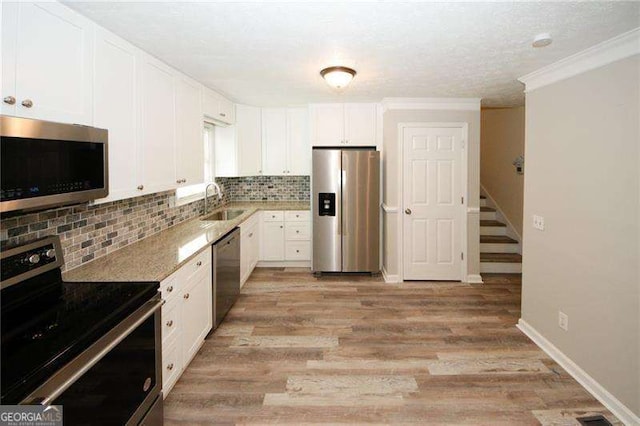 kitchen with sink, light wood-type flooring, appliances with stainless steel finishes, white cabinets, and backsplash