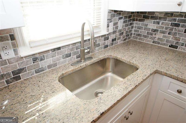 details featuring backsplash, light stone countertops, sink, and white cabinets