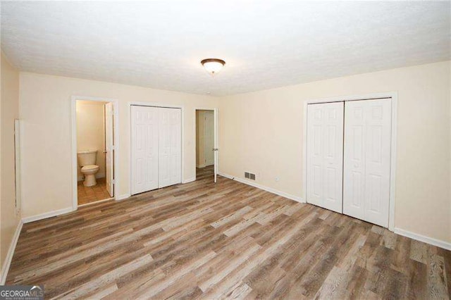 unfurnished bedroom featuring hardwood / wood-style flooring, ensuite bathroom, and two closets