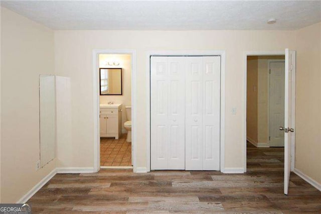 unfurnished bedroom with dark hardwood / wood-style flooring, ensuite bath, and a closet