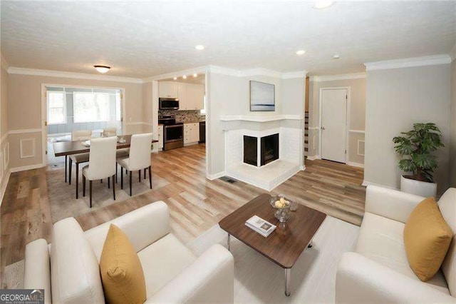 living room featuring crown molding, a fireplace, and light hardwood / wood-style flooring