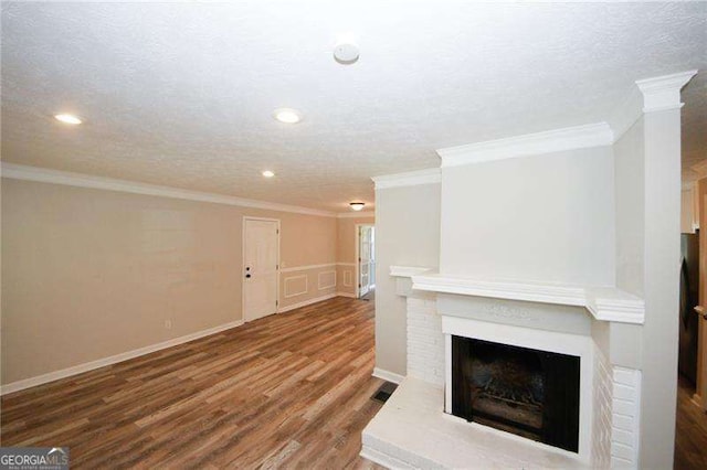 unfurnished living room with hardwood / wood-style floors, crown molding, a textured ceiling, and a brick fireplace