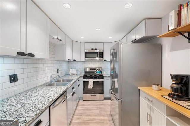 kitchen featuring sink, white cabinetry, stainless steel appliances, tasteful backsplash, and light stone countertops