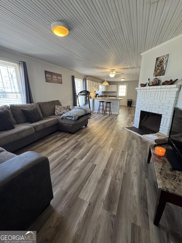 living room with wood-type flooring, a brick fireplace, and crown molding