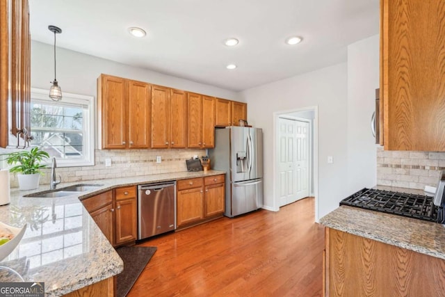 kitchen with appliances with stainless steel finishes, pendant lighting, sink, light stone countertops, and light wood-type flooring