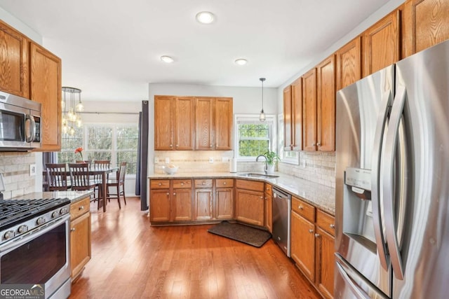 kitchen with sink, decorative light fixtures, appliances with stainless steel finishes, a wealth of natural light, and light stone countertops