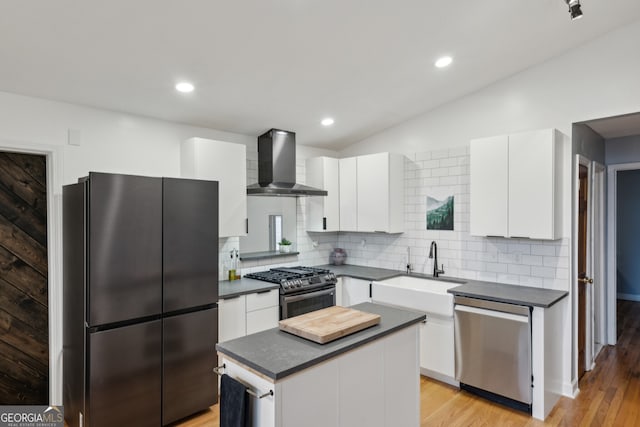 kitchen with appliances with stainless steel finishes, dark countertops, a sink, and wall chimney exhaust hood